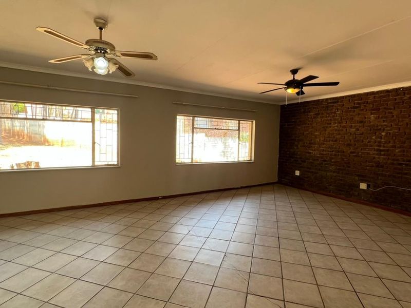 Spacious living area featuring tiled flooring, an exposed brick feature wall, and dual ceiling fans, offering a versatile blank canvas for your interior design.
