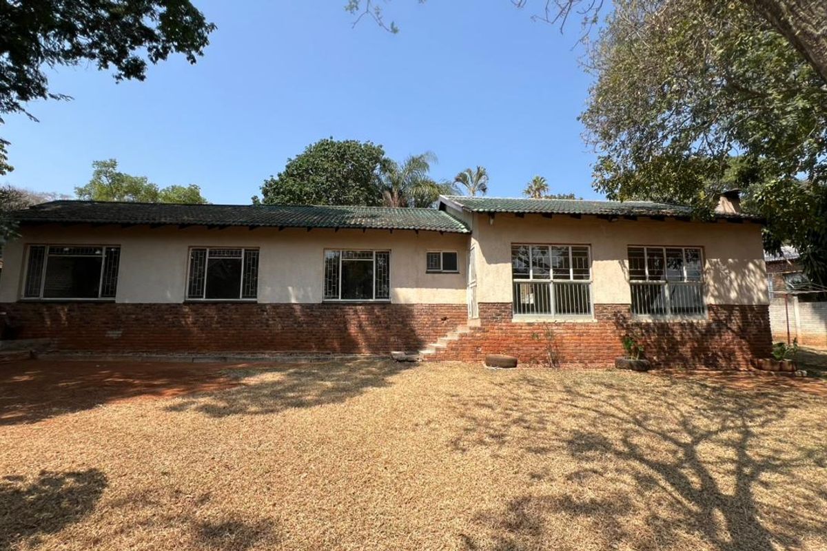 Rear view of a single-story house featuring a brick and plaster facade, tiled roof, and steel-framed windows with security bars.