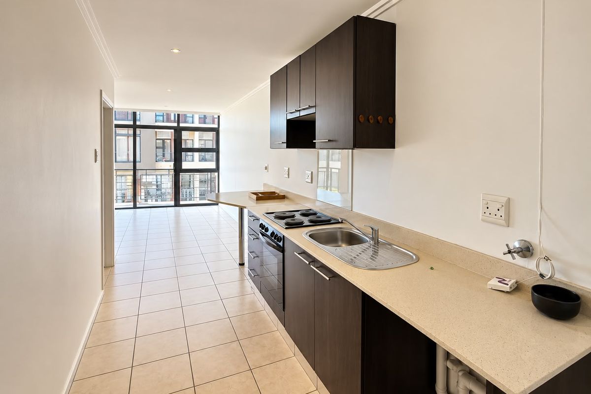 A clean, modern kitchen featuring dark cabinetry, stone countertops, and integrated appliances, leading into an open-plan living area with large glass doors.