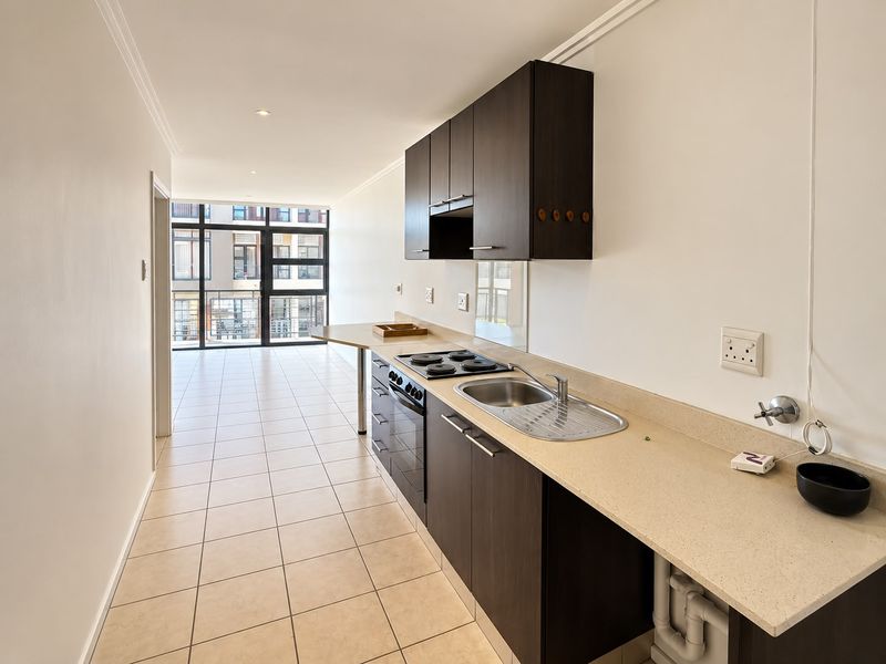 A clean, modern kitchen featuring dark cabinetry, stone countertops, and integrated appliances, leading into an open-plan living area with large glass doors.