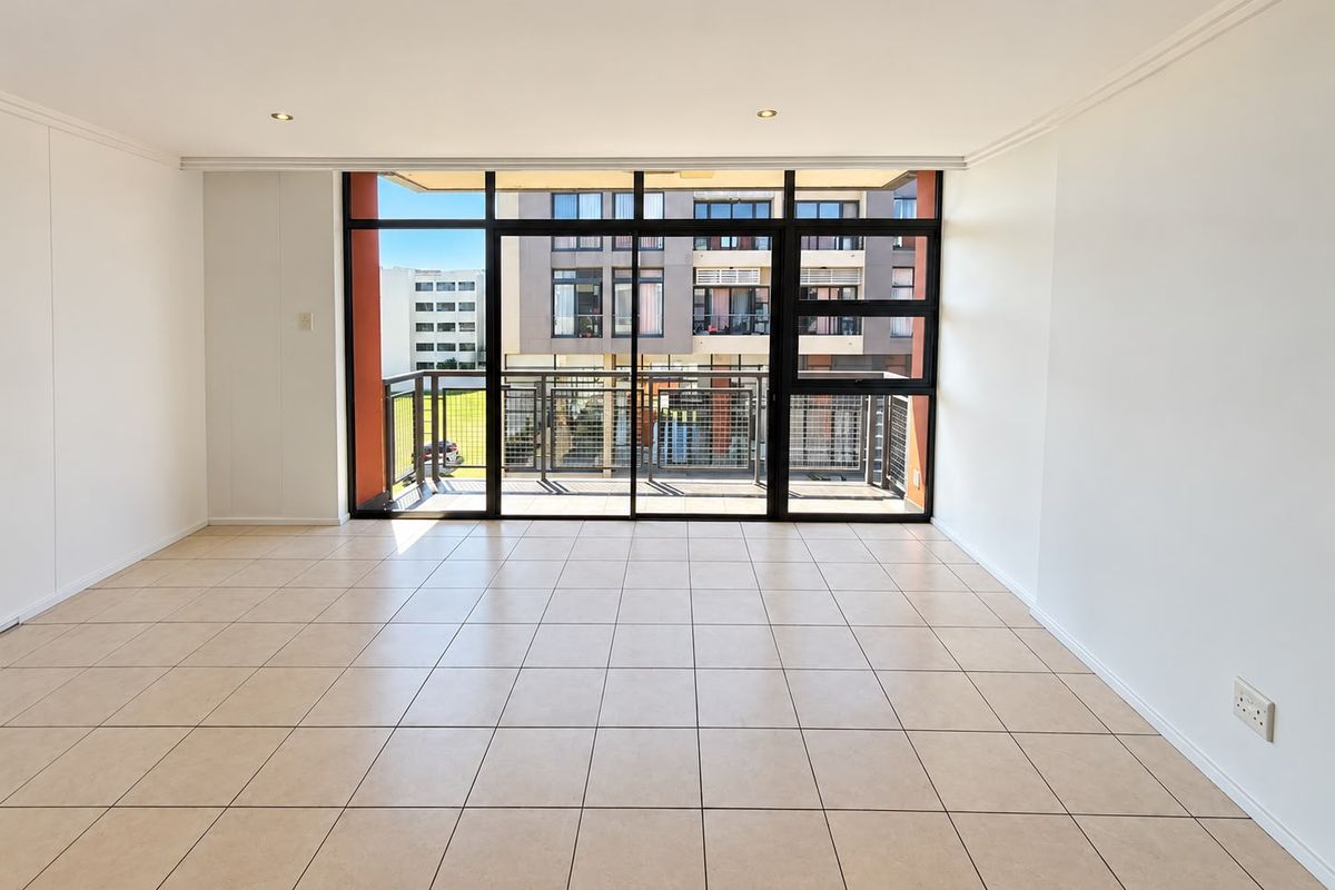A bright and spacious open-plan living area featuring neutral tiled flooring, recessed lighting, and large sliding doors leading to a private balcony.