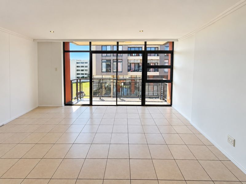 A bright and spacious open-plan living area featuring neutral tiled flooring, recessed lighting, and large sliding doors leading to a private balcony.