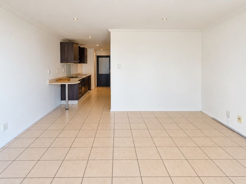 An open-plan living area featuring tiled flooring, recessed lighting, and a compact kitchen with built-in cabinetry, oven, and hob.