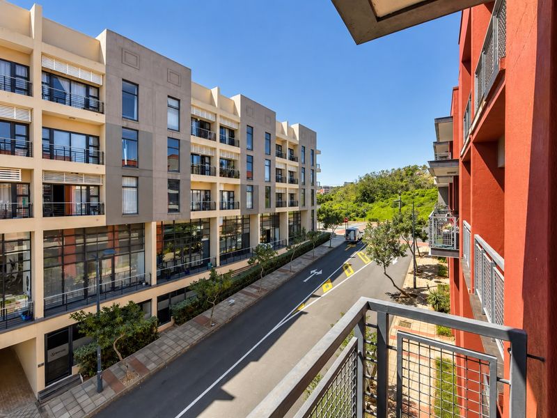 An elevated view from a balcony overlooking a modern apartment complex, street, and surrounding greenery.