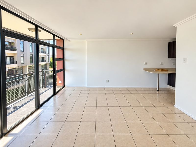 Spacious open-plan living area featuring neutral tiled flooring, recessed lighting, and large sliding glass doors leading to a private balcony.
