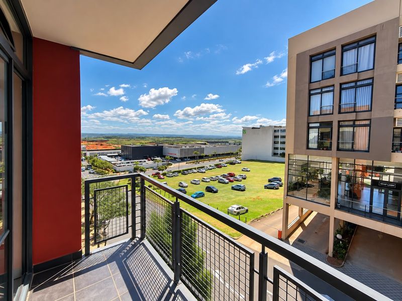 A modern apartment balcony featuring tiled flooring and a metal safety railing, offering an elevated view of the surrounding neighborhood and parking area.