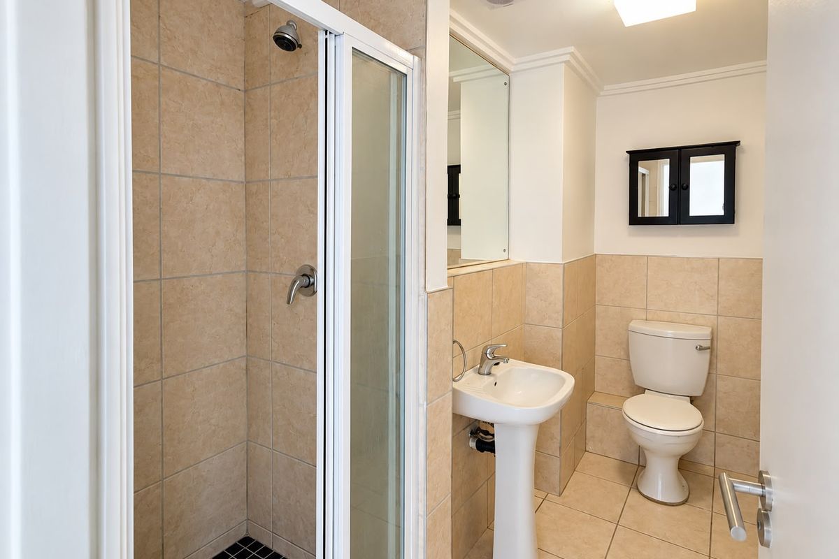 A clean and functional bathroom featuring a shower enclosure, pedestal basin, and toilet with neutral wall and floor tiling.
