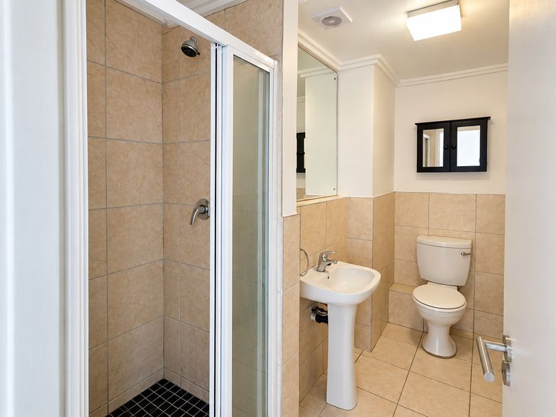 A clean and functional bathroom featuring a shower enclosure, pedestal basin, and toilet with neutral wall and floor tiling.
