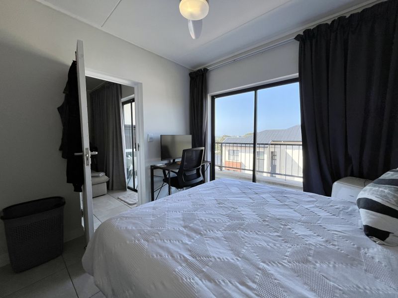A bright bedroom featuring tiled flooring, a ceiling fan, and a sliding glass door that opens onto a private balcony.