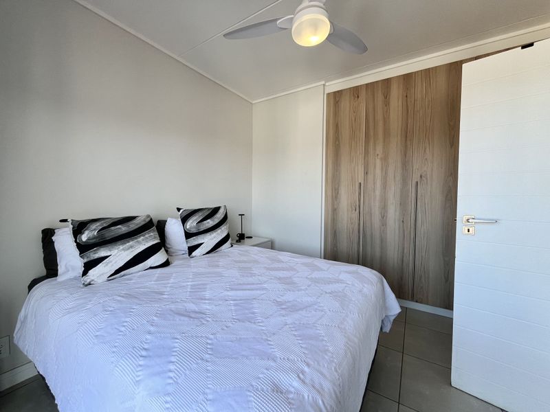 A well-maintained bedroom featuring modern wood-finish built-in cupboards, a ceiling fan, and neutral tiled flooring.