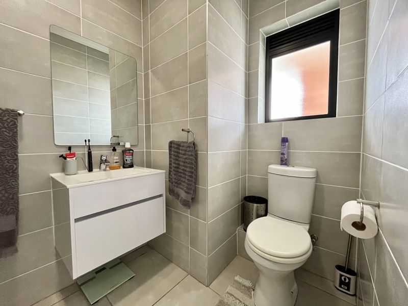 Modern bathroom featuring a wall-mounted vanity, ceramic basin, toilet, and neutral floor-to-ceiling wall tiles with a window for natural light.