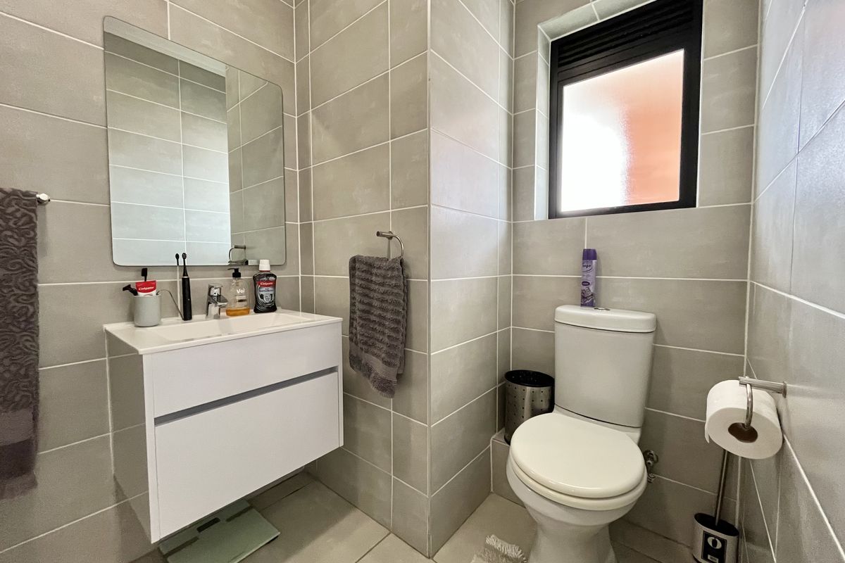 Modern bathroom featuring a wall-mounted vanity, ceramic basin, toilet, and neutral floor-to-ceiling wall tiles with a window for natural light.