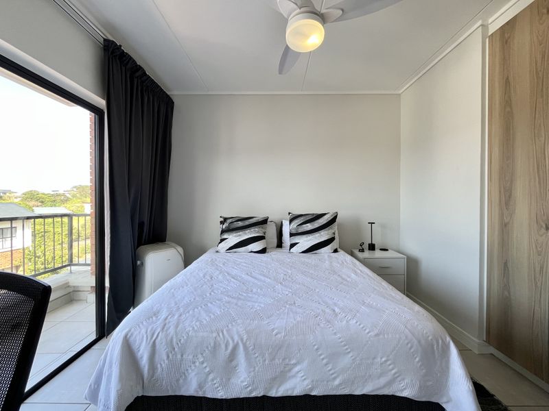 A well-maintained bedroom featuring a ceiling fan, built-in wardrobe, and large sliding glass doors providing access to a private balcony.