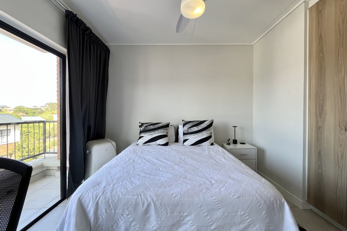 A well-maintained bedroom featuring a ceiling fan, built-in wardrobe, and large sliding glass doors providing access to a private balcony.