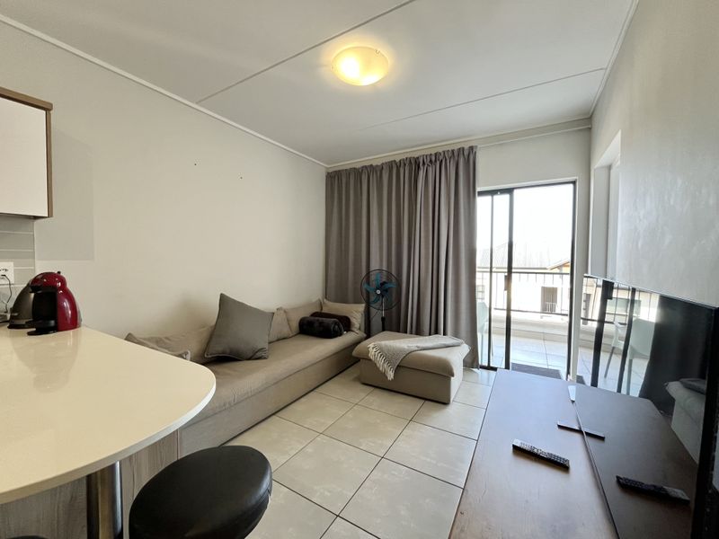 Open-plan living area featuring tiled flooring, a breakfast counter, and direct access to a balcony through a sliding glass door.