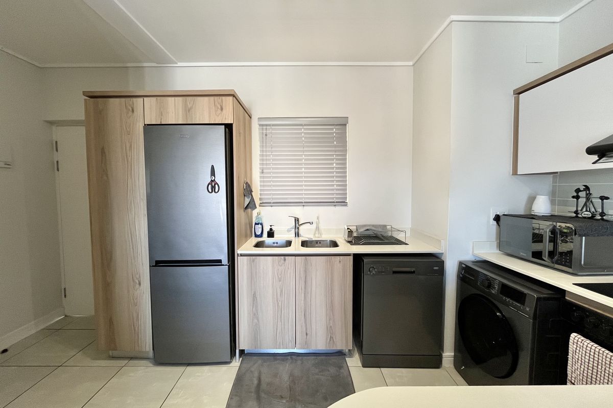 A functional kitchen featuring light wood-finish cabinetry, a double sink with mixer tap, tiled flooring, and integrated space for appliances.