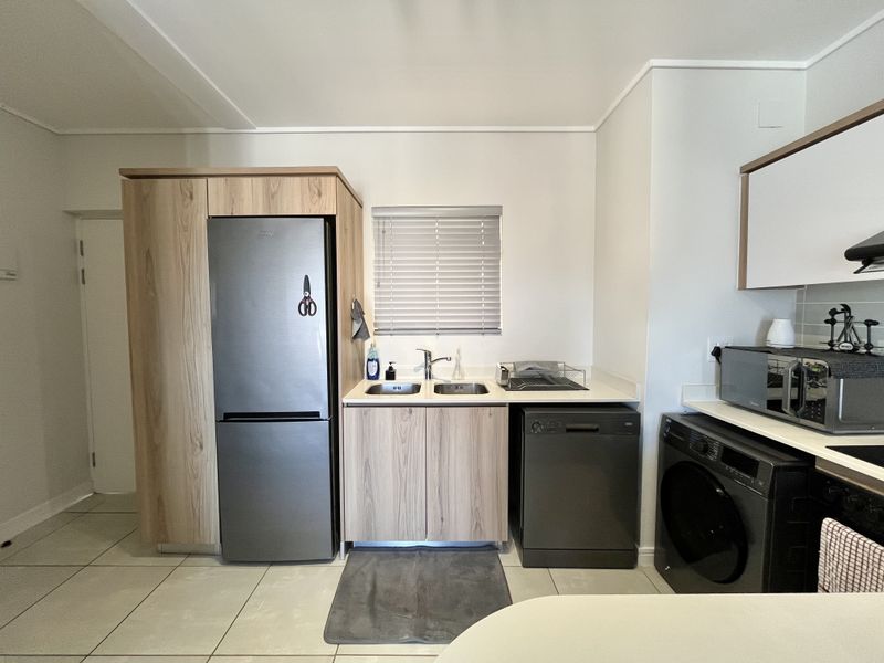 A functional kitchen featuring light wood-finish cabinetry, a double sink with mixer tap, tiled flooring, and integrated space for appliances.