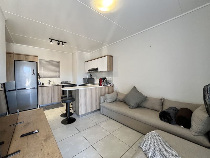 An open-plan living and kitchen area featuring modern wood-look cabinetry, a breakfast bar, tiled flooring, and a functional layout suitable for compact apartment living.