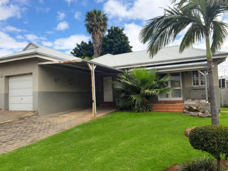 Front elevation of a townhouse featuring a single garage, attached carport, paved driveway, and a well-maintained front garden with established landscaping.