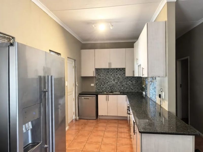 A functional kitchen featuring granite countertops, mosaic tile backsplash, ample built-in cabinetry, and ceramic floor tiles.