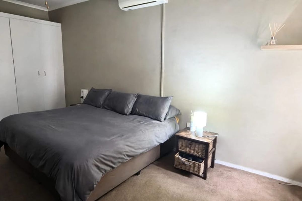 A bedroom featuring built-in cupboards, a wall-mounted air conditioning unit, and a floating shelf, finished with carpeted flooring.