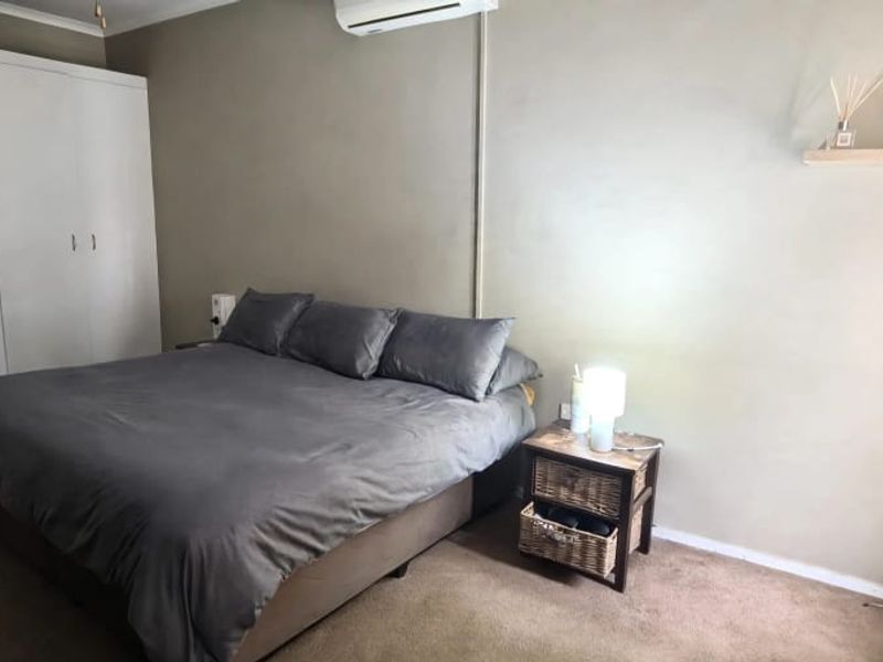 A bedroom featuring built-in cupboards, a wall-mounted air conditioning unit, and a floating shelf, finished with carpeted flooring.