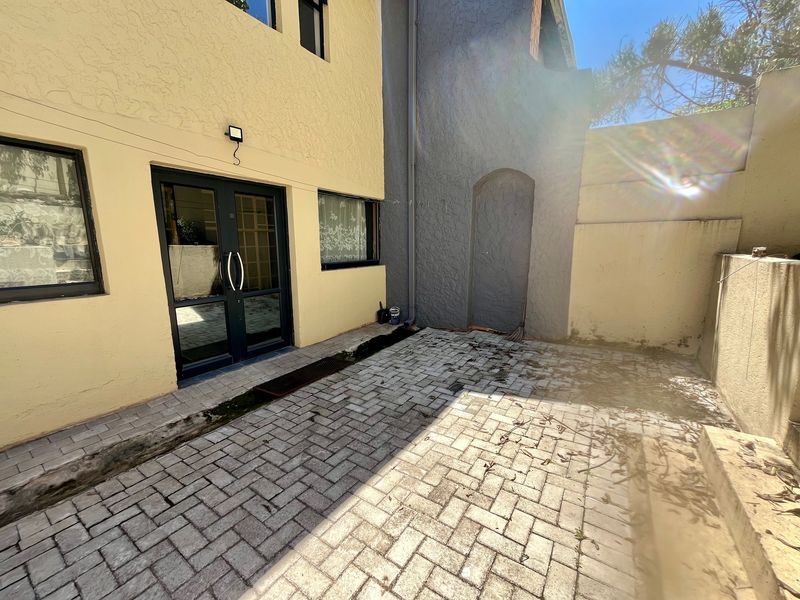 A paved rear courtyard area featuring double glass doors, exterior wall lighting, and a textured wall finish, offering a private outdoor space.
