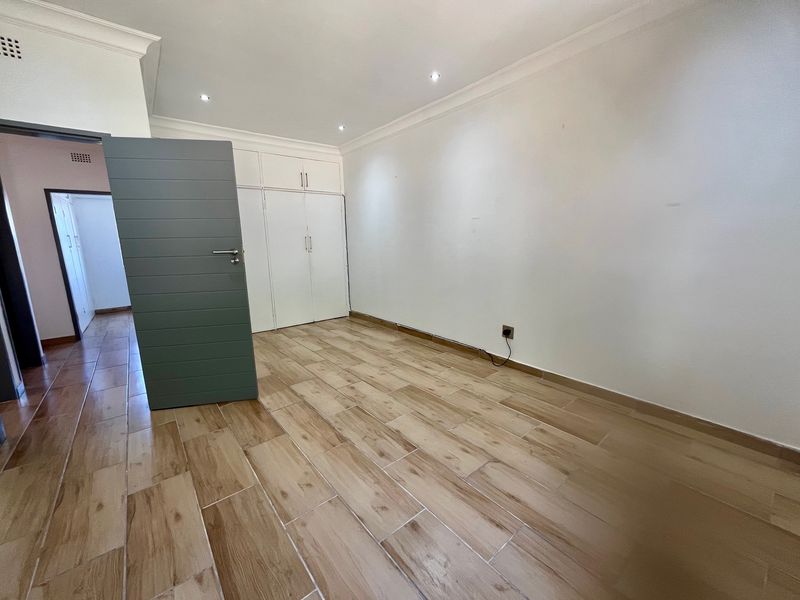A bright, empty bedroom featuring modern wood-look tile flooring, built-in cupboards, and recessed downlighting.