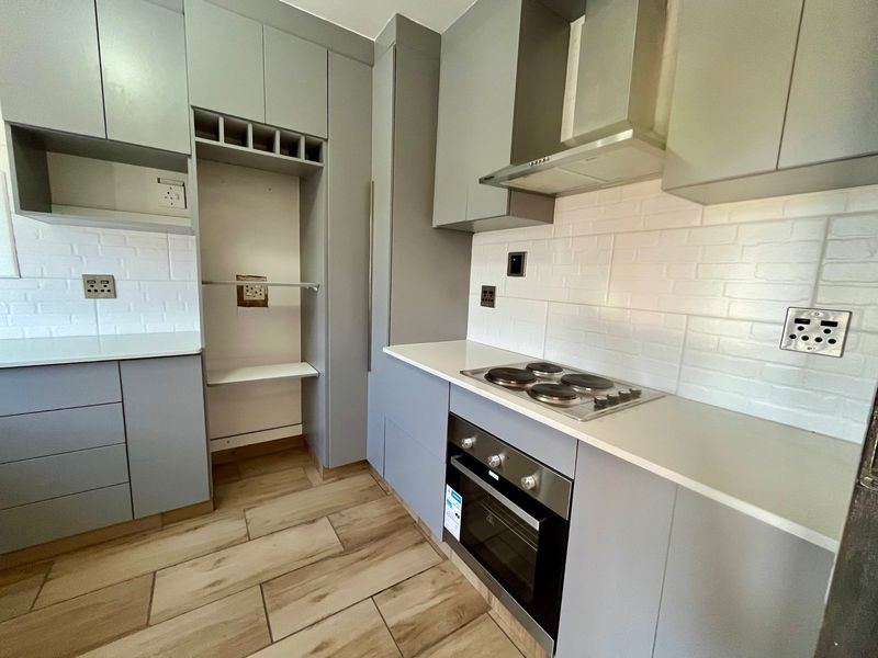 Modern kitchen featuring grey cabinetry, stone countertops, subway tile backsplash, and integrated stainless steel appliances including an oven and electric hob.