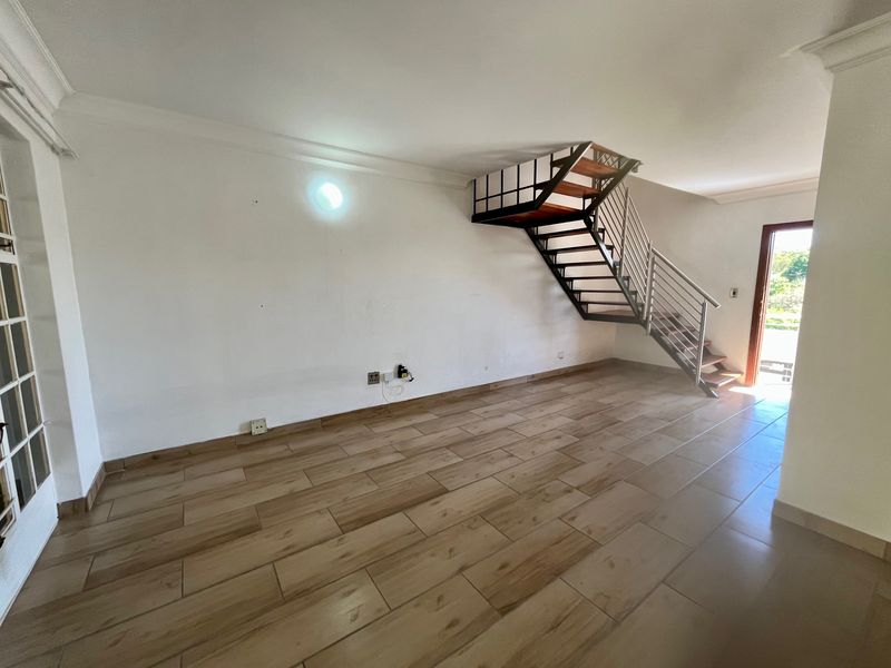 An open-plan living area featuring wood-look tile flooring, a modern metal staircase with wooden treads, and direct access to an outdoor space.