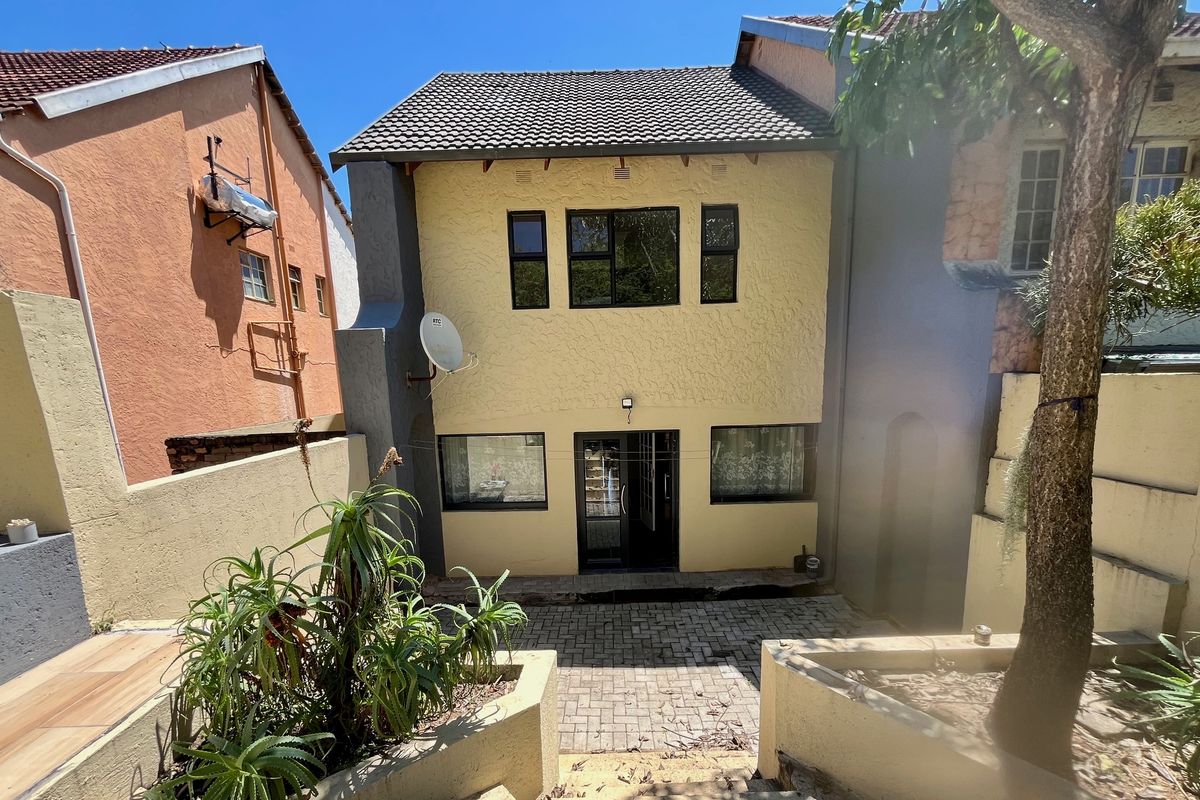 Rear view of a two-story house featuring a paved courtyard, raised garden beds, and a tiled roof with aluminium window frames.