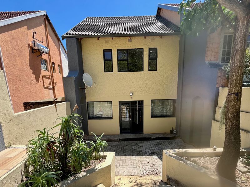 Rear view of a two-story house featuring a paved courtyard, raised garden beds, and a tiled roof with aluminium window frames.