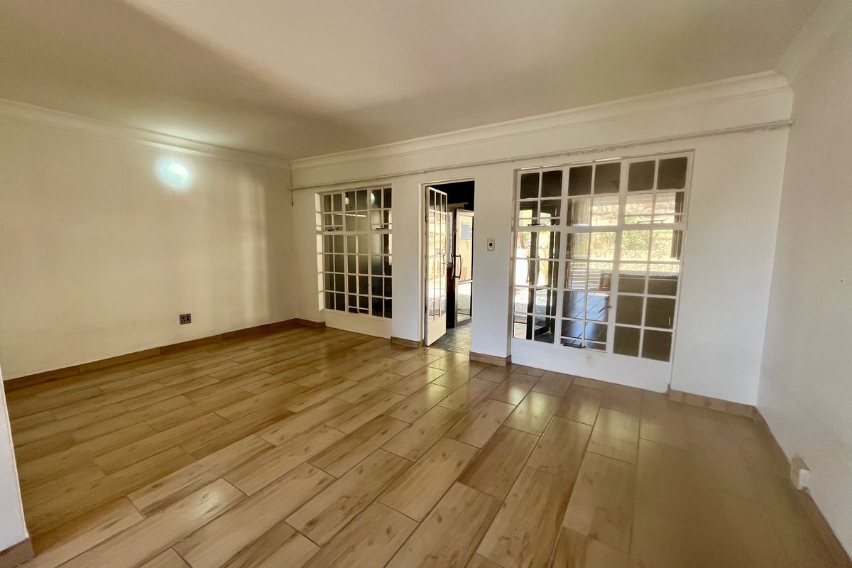 Spacious, empty living area featuring wood-look tile flooring, coved cornicing, and multiple sets of glass-paned french doors providing natural light.