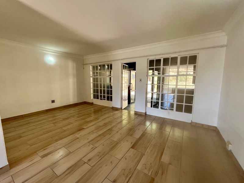 Spacious, empty living area featuring wood-look tile flooring, coved cornicing, and multiple sets of glass-paned french doors providing natural light.