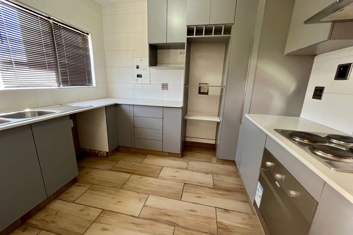 Modern kitchen featuring grey cabinetry, white countertops, subway tile backsplash, wood-look tiled flooring, and integrated appliances including an oven and hob.