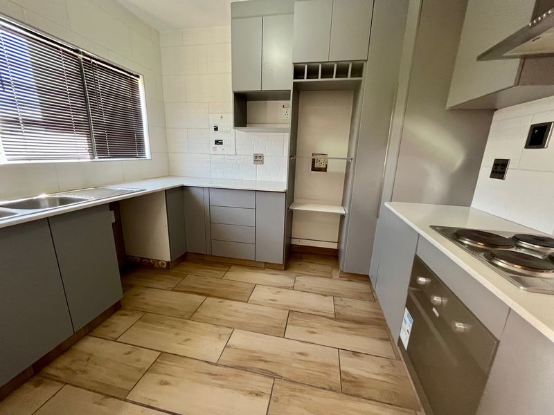 Modern kitchen featuring grey cabinetry, white countertops, subway tile backsplash, wood-look tiled flooring, and integrated appliances including an oven and hob.
