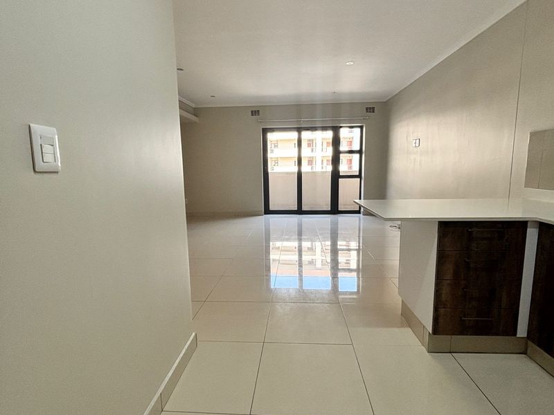 Spacious open-plan living area featuring large format floor tiles, a modern kitchen peninsula, and sliding glass doors leading to a balcony.