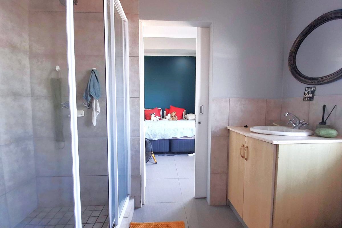 A functional bathroom featuring a shower enclosure, vanity cabinet with basin, and neutral wall and floor tiling, with an adjoining bedroom visible.