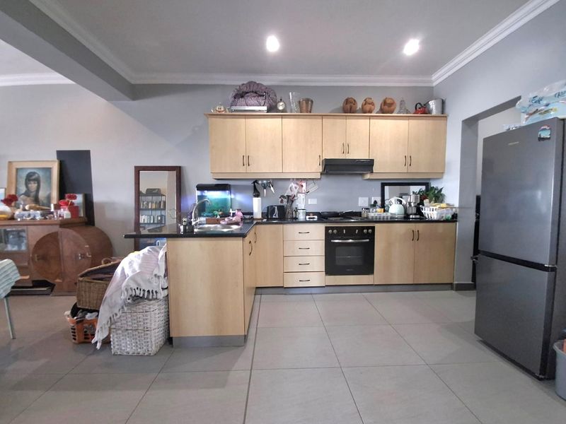 A functional kitchen featuring light wood cabinetry, dark countertops, built-in oven, extractor fan, and neutral floor tiles in an open-plan layout.