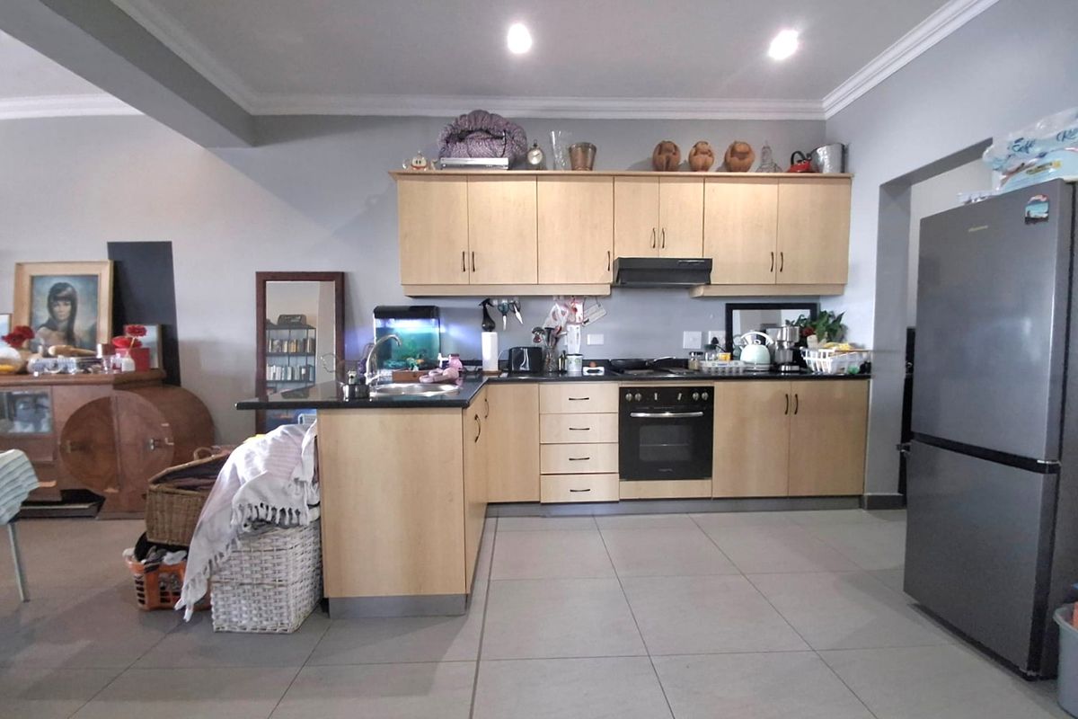 A functional kitchen featuring light wood cabinetry, dark countertops, built-in oven, extractor fan, and neutral floor tiles in an open-plan layout.