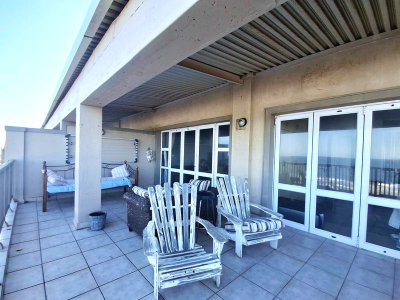 A spacious covered balcony featuring tiled flooring, corrugated metal ceiling, and large sliding glass doors providing access to the interior living space.
