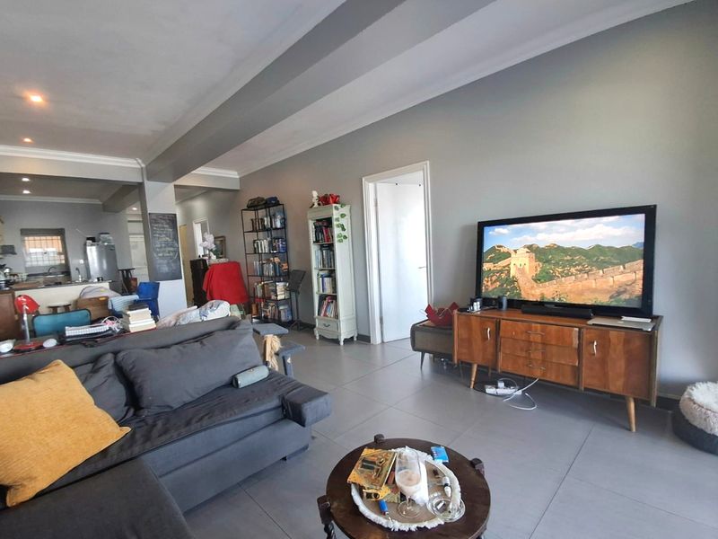 Spacious open-plan living area featuring neutral grey walls, tiled flooring, and recessed lighting, seamlessly connecting to the kitchen space.