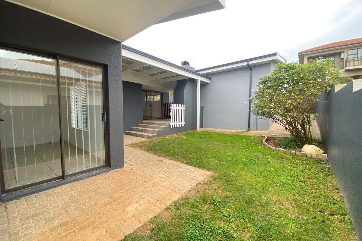 A well-maintained rear garden featuring a paved patio area, a covered outdoor space, and a neat lawn with established landscaping.