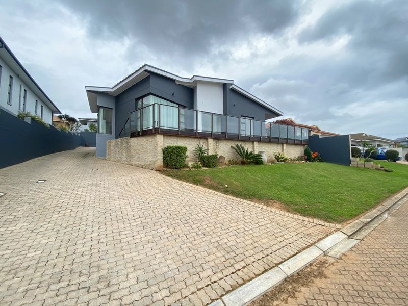 Modern residential exterior featuring a paved driveway, stone-clad retaining wall, and a raised deck with a glass balustrade.