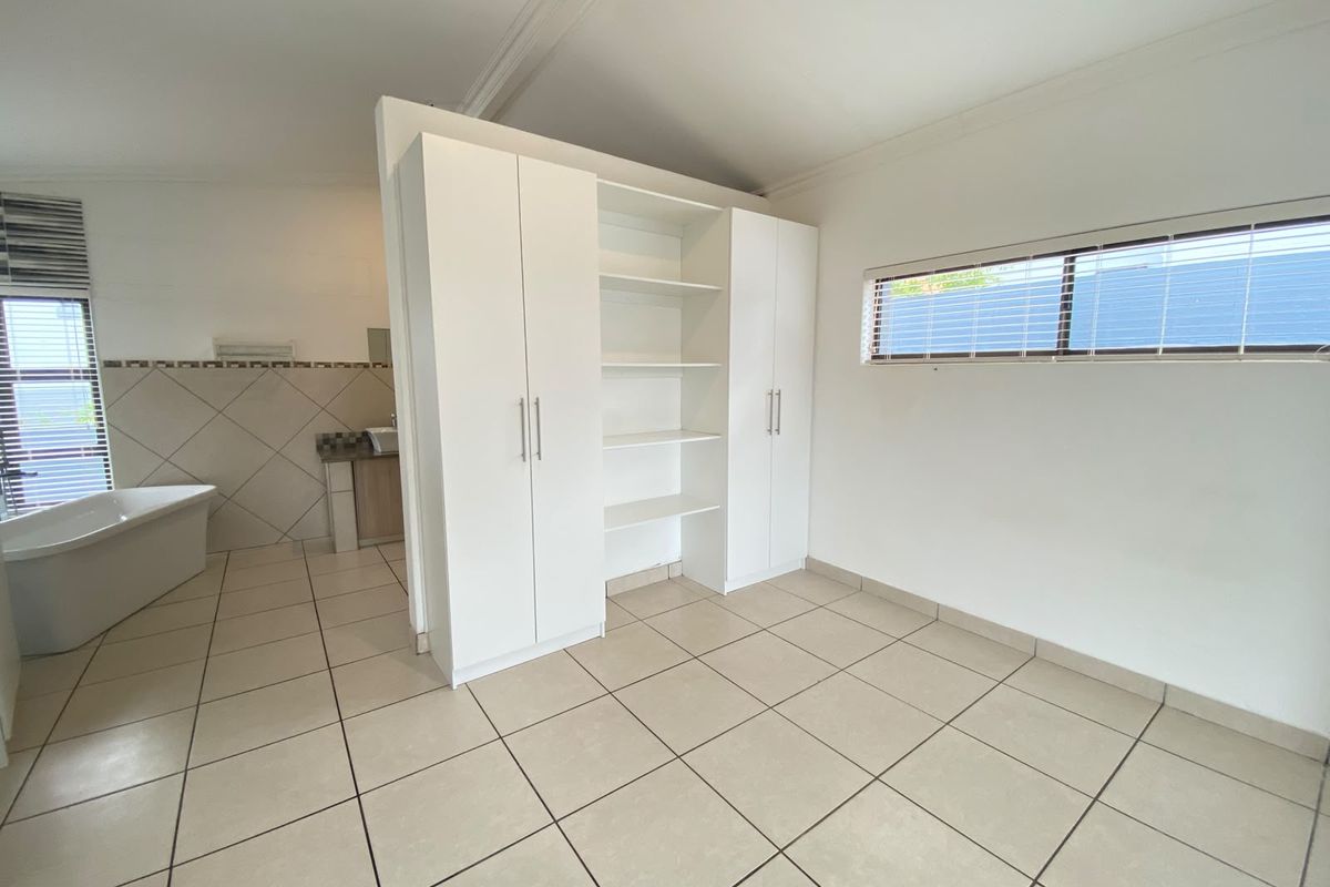 Spacious bedroom featuring neutral tiled flooring, built-in storage cabinetry, and an open-plan en-suite bathroom area with a modern freestanding bathtub.
