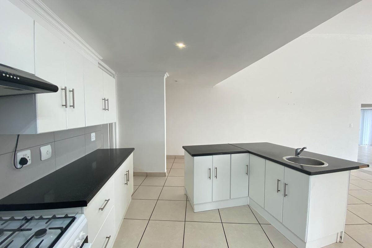 A clean, modern kitchen featuring white cabinetry, contrasting black granite countertops, a central island with a sink, and tiled flooring throughout.