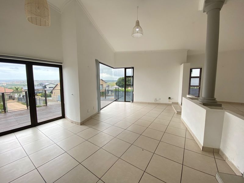 Spacious open-plan living area featuring neutral tiled flooring, a prominent structural column, and large glass sliding doors opening onto an outdoor deck.