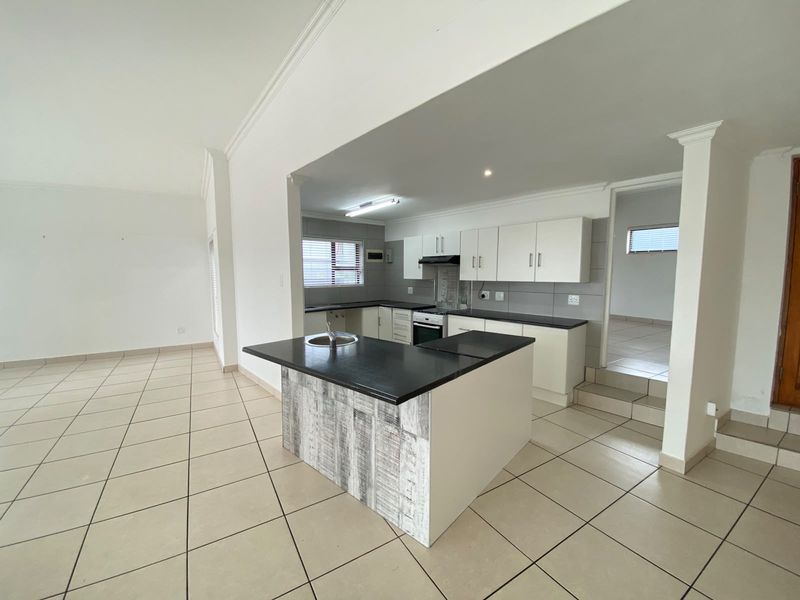Open plan kitchen featuring a central island, built-in cabinetry, tiled flooring, and a functional layout connecting to the living area.