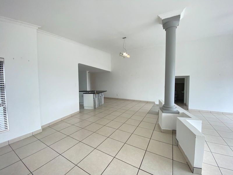 Spacious open-plan living area featuring tiled flooring, a decorative column, and a functional kitchen island with built-in cabinetry.