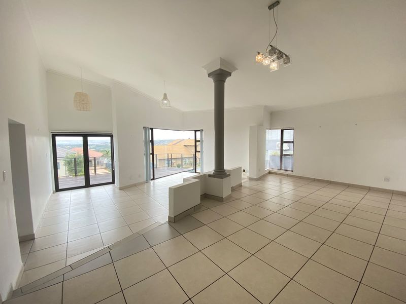 Spacious open-plan living area featuring tiled floors, a central structural column, and large sliding glass doors leading to an outdoor balcony with scenic views.